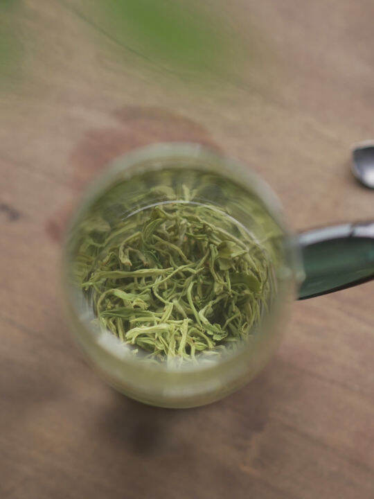 A steaming cup of light green Gaoshan Cha, with tea leaves visible at the bottom.